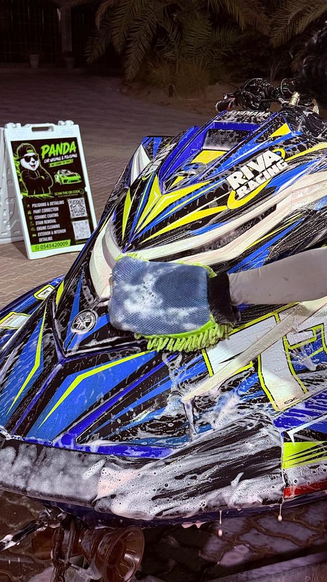 Blue and yellow Yamaha jet ski being hand-washed with a wash mitt beside a Panda Car Wash sign